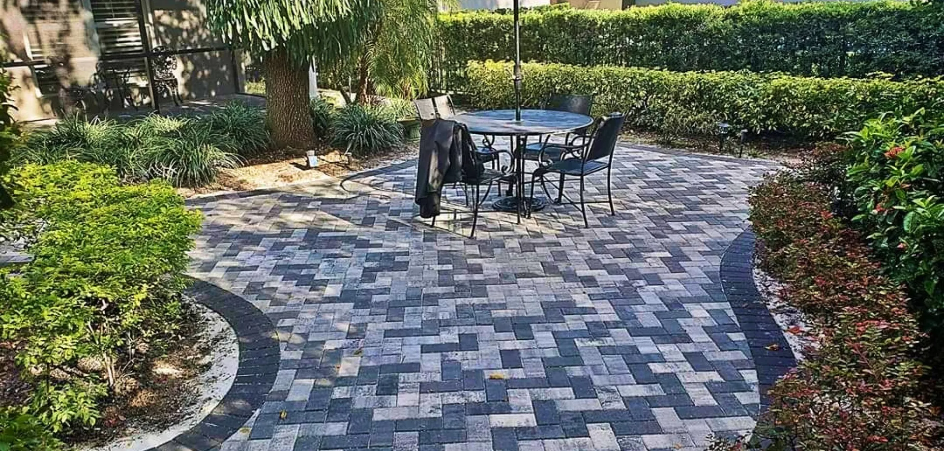 Circular herringbone paver patio with a bistro table and hedges